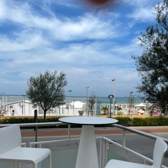 Vista mare con tavolo e sedie bianche, cielo azzurro.