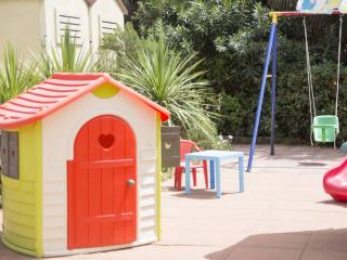 Spielbereich für Kinder mit Spielhaus, Schaukel und Rutsche im Freien.