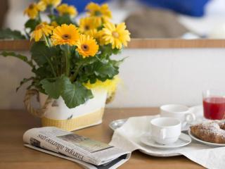 Frühstück mit Blumen, Zeitung, Saft und Gebäck auf einem Tisch.