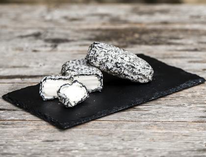 Formaggio caprino con crosta di cenere su piatto di ardesia.