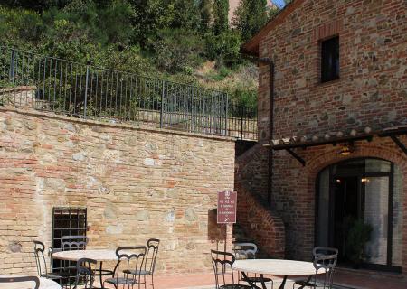 Cortile soleggiato con tavoli in ferro, mura antiche e natura rigogliosa.