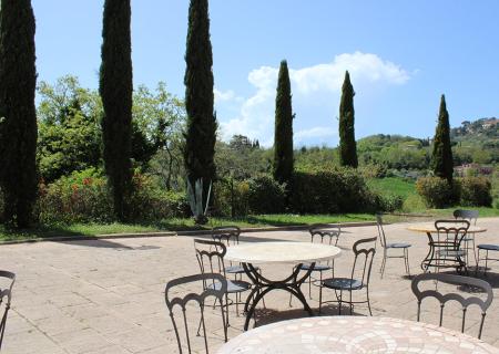Tavolini all'aperto con vista su cipressi e colline toscane sotto un cielo sereno.