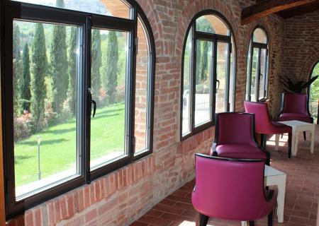 Sala luminosa con archi in mattoni, sedie viola e vista su cipressi.