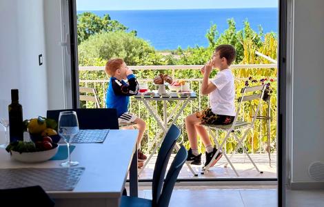 Due bambini fanno colazione su un balcone con vista mare.