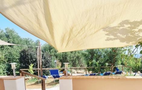 Tenda beige ombreggia un giardino sereno con sedie blu e verde rigoglioso.