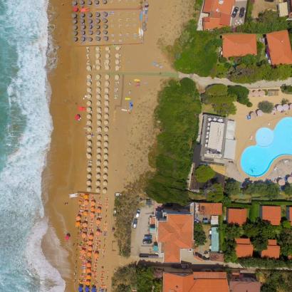 Spiaggia dorata, ombrelloni colorati, mare agitato, piscina invitante, atmosfera estiva.