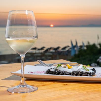 Tramonto sul mare, calice di vino bianco, piatto di pasta nera elegante.