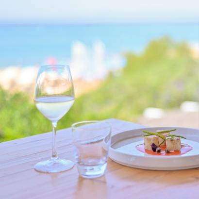 Vista mare, piatto gourmet e calice di vino su tavolo luminoso.