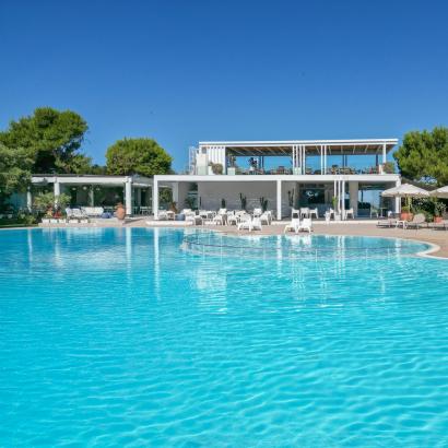 Piscina luminosa con cielo blu, ombrelloni e relax estivo.