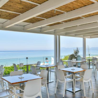 Terrazza sul mare con tavoli bianchi, atmosfera rilassante e vista mozzafiato.
