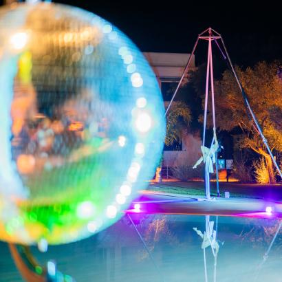 Spettacolo notturno con acrobata su tessuti, luci colorate e riflessi sull'acqua.