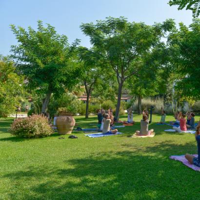 Persone praticano yoga all'aperto, circondate da alberi e natura rigogliosa.