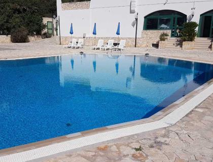 Piscina tranquilla con lettini e ombrelloni blu, atmosfera rilassante e soleggiata.