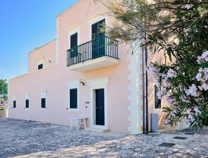 Casa rosa con balcone, fiori e cielo azzurro, atmosfera serena e accogliente.