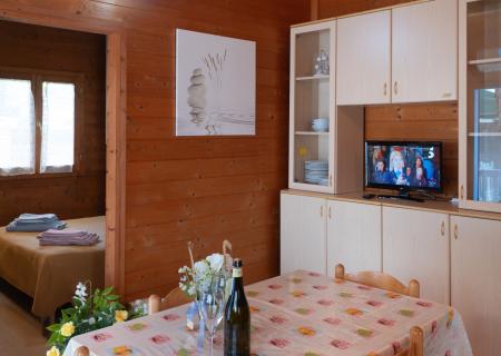 Cozy wooden living room with set table, flowers, and TV on.