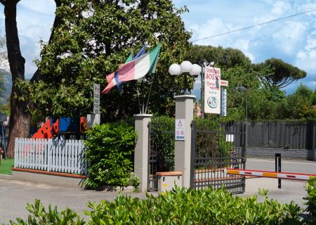 Campsite entrance with flags, lush nature, and a clear sky.