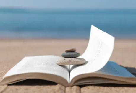 Libro sulla spiaggia con sassi sopra, mare sullo sfondo.