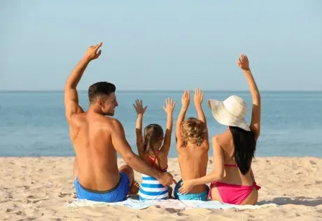 Famiglia in spiaggia, seduta sulla sabbia, braccia alzate verso il mare.