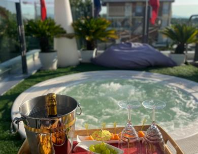 Champagne e frutta fresca accanto a una vasca idromassaggio su terrazza soleggiata.