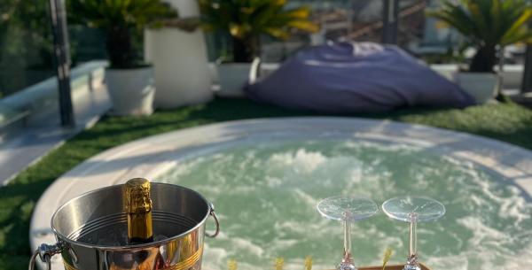 Champagne e frutta fresca accanto a una vasca idromassaggio su terrazza soleggiata.