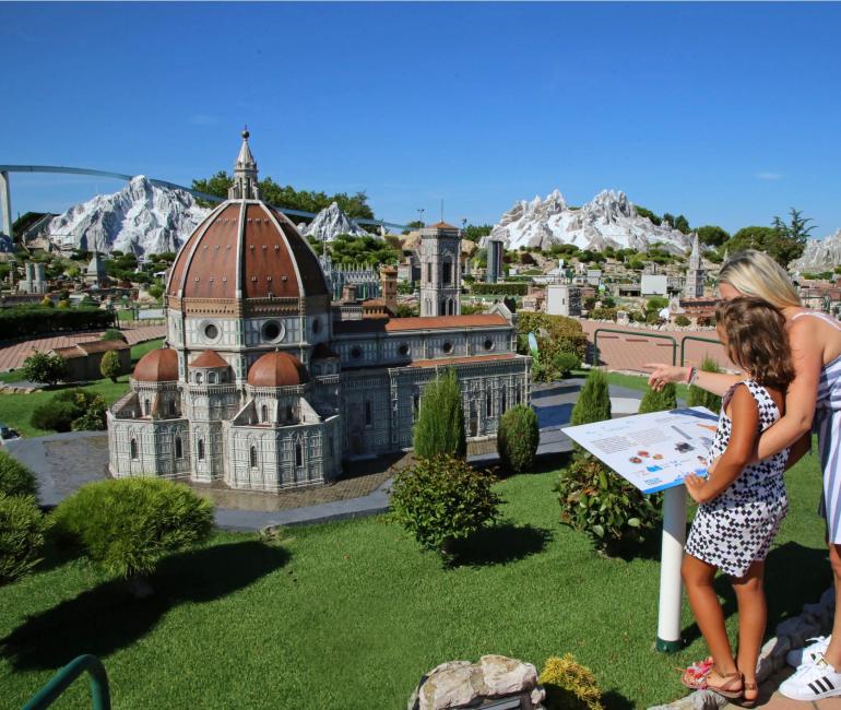 Due persone osservano un modello in miniatura di una cattedrale con montagne sullo sfondo.