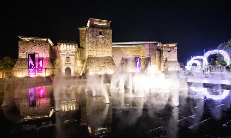 Castello illuminato di notte con fontane e giochi di luce.