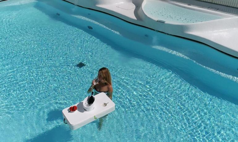 Frau trinkt im Pool mit einem schwimmenden Tisch.