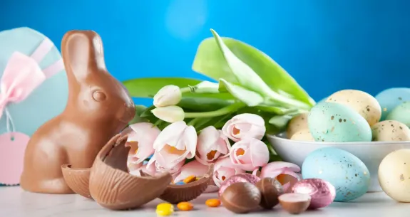 Chocolate bunny, colorful eggs, and tulips on a blue background.