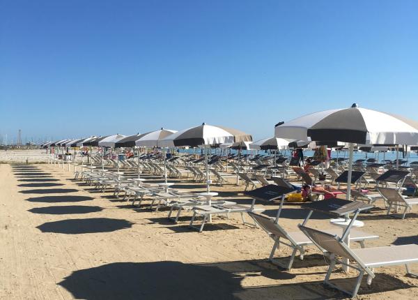 Spiaggia serena, ombrelloni allineati, mare calmo sotto un cielo azzurro.