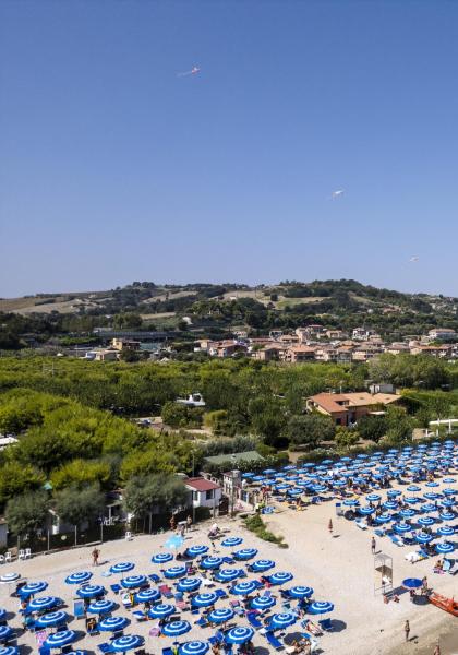 Spiaggia affollata con ombrelloni blu, mare e colline sullo sfondo.