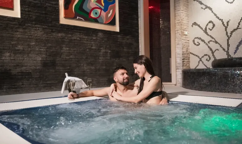 Couple détendu dans un jacuzzi avec champagne et art moderne.