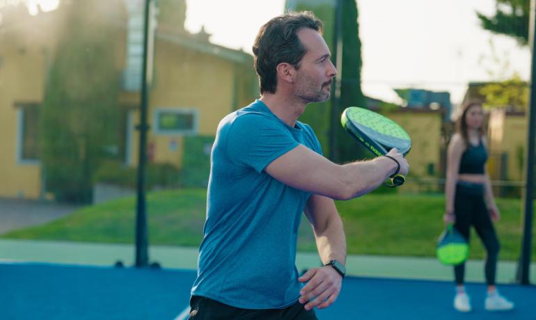 Uomo gioca a padel all'aperto con racchetta verde.