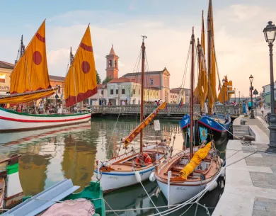 Barche storiche con vele colorate su un canale al tramonto.