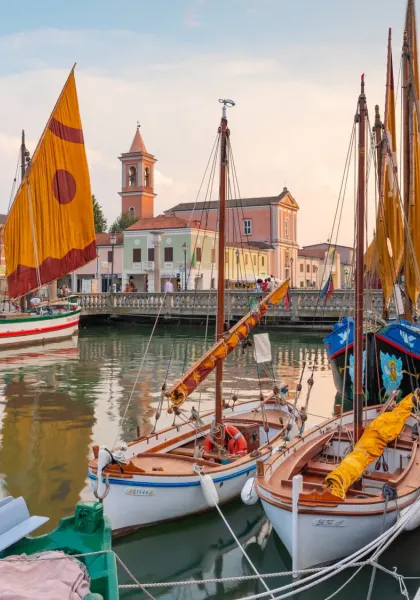 Historic boats with colorful sails on a canal at sunset.