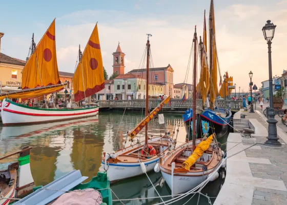 Barche storiche con vele colorate su un canale al tramonto.