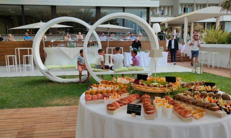 Fête en plein air avec buffet, gens qui discutent et enfants qui jouent.