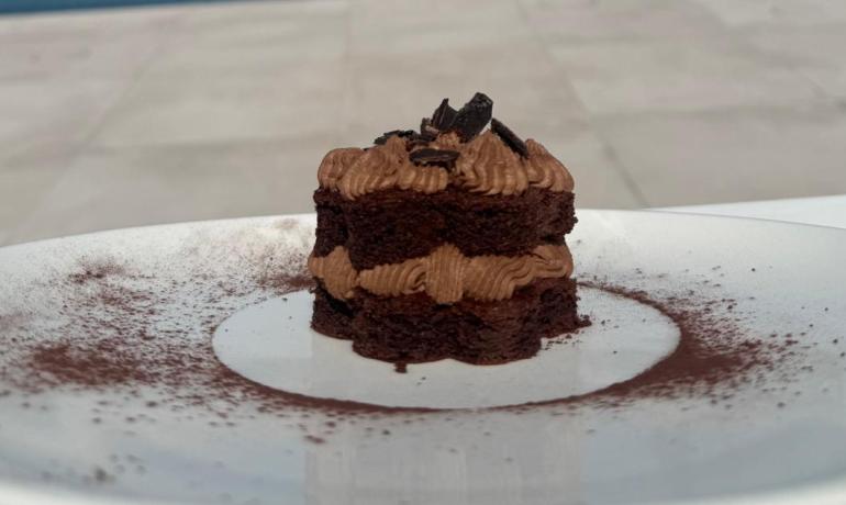 Piccolo dolce al cioccolato, mare e piscina in lontananza, giornata serena.