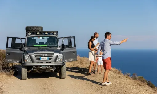 Gruppo osserva il mare accanto a un fuoristrada su una strada sterrata.