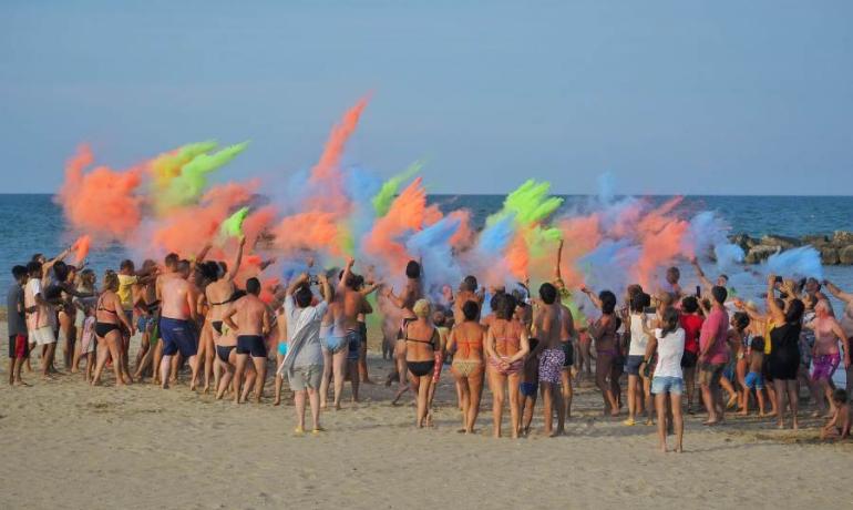 Gente in spiaggia lancia polveri colorate durante una festa.