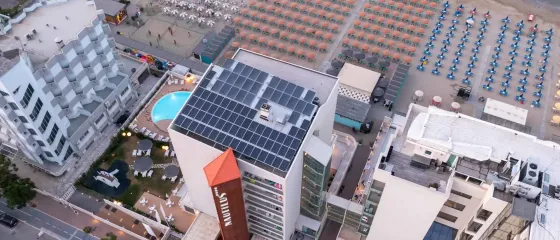 Vista aerea di un hotel moderno vicino a una spiaggia affollata di ombrelloni.