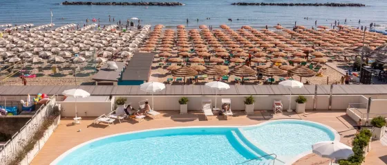 Spiaggia affollata, ombrelloni colorati e piscina rinfrescante, atmosfera estiva vivace.