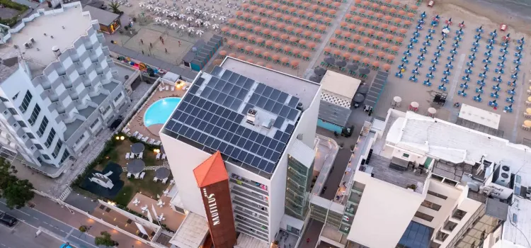 Vista aerea di un hotel moderno vicino a una spiaggia affollata di ombrelloni.