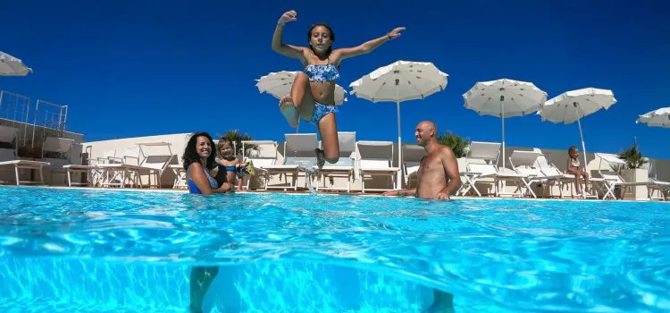 Bambina salta in piscina, famiglia felice sotto il sole estivo.