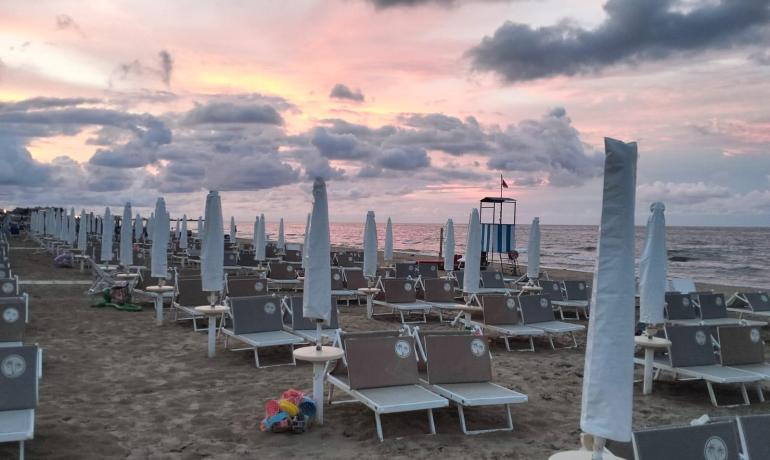 Spiaggia al tramonto con ombrelloni chiusi e lettini vuoti.