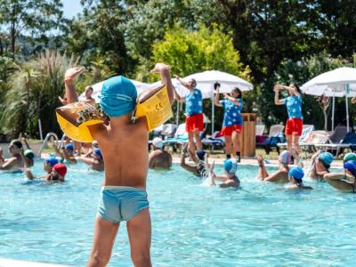 Bambino in piscina con braccioli, animatori sullo sfondo.