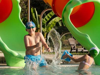 Bambini giocano in piscina con scivolo colorato.