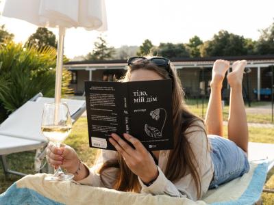 Donna legge un libro su una sdraio con un bicchiere di vino.