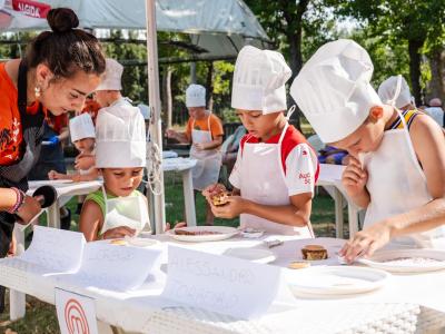 Bambini cucinano sotto un ombrellone durante un evento MasterChef Junior.