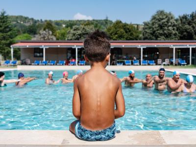 Kind beobachtet lächelnde Menschen im Pool unter der Sommersonne.