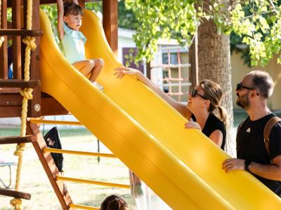 Kinder spielen fröhlich auf der Rutsche, lächelnde Eltern schauen zu.
